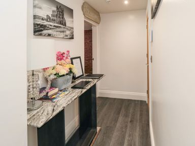 A hallway with a marble top console table holding a lamp flowers and books at Tower Apartment in Whitby