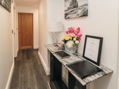 A hallway with a marble top console table holding flowers books a lamp and a framed certificate at Tower Apartment in Whitby