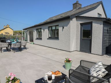 An outdoor patio with a dining table and chairs set near a house with grey walls and windows at Rhiwmynach in Pontarfynach near Aberystwyth