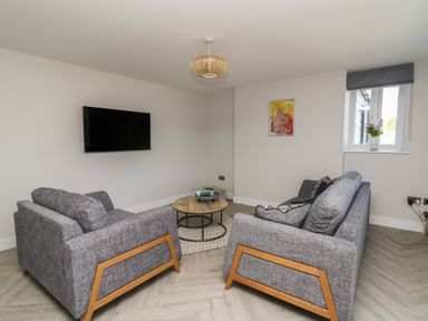 A living room with two gray sofas a round wooden coffee table a wall-mounted TV a window with a flower vase and a framed picture on the wall at Rhiwmynach in Pontarfynach near Aberystwyth