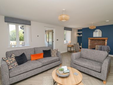 A living room with two gray sofas a round wooden coffee table and a fireplace with a blue accent wall at Rhiwmynach in Pontarfynach near Aberystwyth