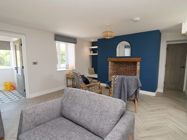 A living room with a gray sofa two patterned chairs a blue accent wall with a brick fireplace and mirror at Rhiwmynach in Pontarfynach near Aberystwyth