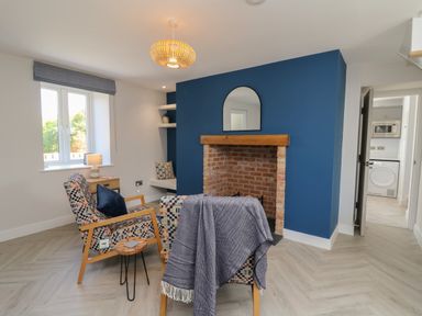 A living room with two patterned chairs a small wooden side table a brick fireplace with a wooden mantel and a mirror above it at Rhiwmynach in Pontarfynach near Aberystwyth