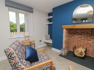 A seating area with patterned armchairs a side table with a lamp a window a built in corner bench and a brick fireplace with log storage at Rhiwmynach Pontarfynach near Aberystwyth