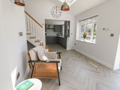 A sitting area with a chair and a small table with a book near a staircase and a kitchen in the background at Rhiwmynach in Pontarfynach near Aberystwyth