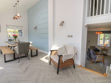 An open dining area with a wooden table and benches next to a light blue patterned wall and a lounge area with armchairs and a window at Rhiwmynach Pontarfynach near Aberystwyth
