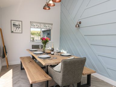 A dining area with a wooden table and bench set with plates and glasses next to a blue textured wall at Rhiwmynach in Pontarfynach near Aberystwyth
