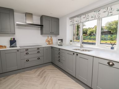 A kitchen with grey cabinets a stainless steel range hood a window with floral blinds and a coffee maker at Rhiwmynach in Pontarfynach near Aberystwyth