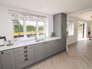 A kitchen with grey cabinets a window with floral blinds and a sink at Rhiwmynach in Pontarfynach near Aberystwyth