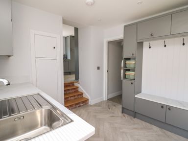 A kitchen area with a stainless steel sink a countertop gray cabinets and a small set of wooden steps leading to another room at Rhiwmynach in Pontarfynach near Aberystwyth