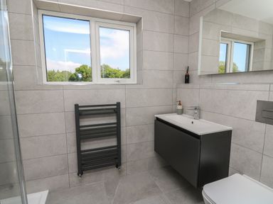 A bathroom with a window a black towel radiator a wall-mounted sink and a toilet at Rhiwmynach in Pontarfynach near Aberystwyth