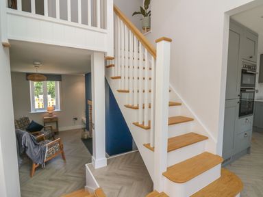 A staircase with wooden steps and white railing next to a living room and a kitchen area at Rhiwmynach in Pontarfynach near Aberystwyth