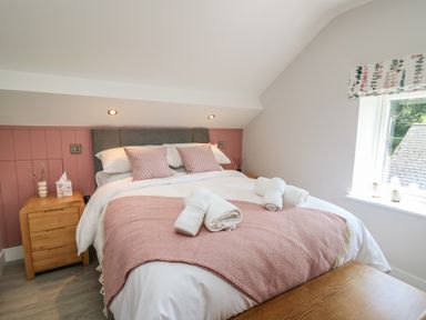 A bedroom with a double bed with pink cushions and blanket bedside tables and a window with a floral blind at Rhiwmynach in Pontarfynach near Aberystwyth