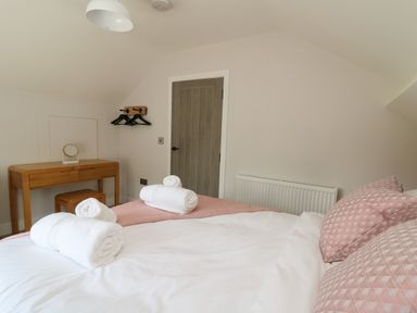 A bedroom with a bed with pink pillows and white towels on it a wooden desk with a small mirror a door and a wall radiator at Rhiwmynach in Pontarfynach near Aberystwyth