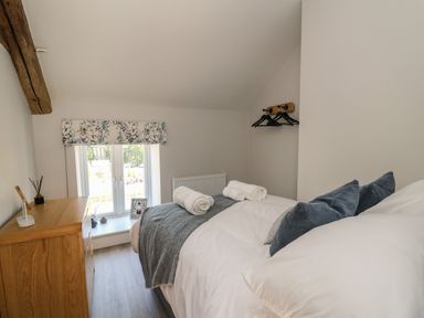 A bedroom with a bed with white linens and blue pillows next to a wooden dresser and a window at Rhiwmynach in Pontarfynach near Aberystwyth