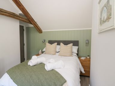 A bedroom with a double bed green blanket beige pillows wooden bedside tables and exposed wooden ceiling beams at Rhiwmynach in Pontarfynach near Aberystwyth