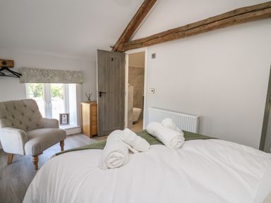 A bedroom with a bed with rolled towels an armchair a wooden dresser and an open door leading to a bathroom at Rhiwmynach in Pontarfynach near Aberystwyth