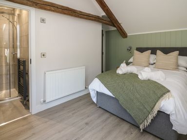 A bedroom with a double bed with beige pillows and a green throw blanket next to a bathroom with a shower at Rhiwmynach in Pontarfynach near Aberystwyth