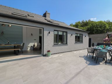 An outdoor patio with a dining table and chairs next to a house with sliding doors and windows at Rhiwmynach in Pontarfynach near Aberystwyth
