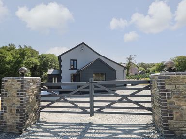 A stone entrance gate with wooden gates and a driveway leading to a house surrounded by trees at Rhiwmynach in Pontarfynach near Aberystwyth