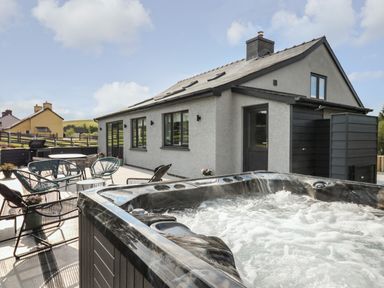 An outdoor patio with a hot tub seating and tables beside a grey house with black windows at Rhiwmynach in Pontarfynach near Aberystwyth