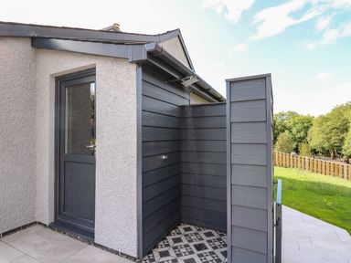 An outdoor shower area with dark wood paneling next to a light textured wall and a door at Rhiwmynach in Pontarfynach near Aberystwyth