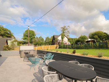 An outdoor patio with a dining table, chairs, lounge chairs, a hot tub, and a fenced garden at Rhiwmynach in Pontarfynach near Aberystwyth