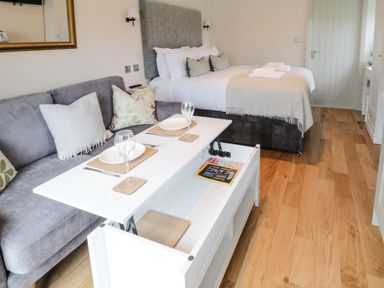 A bedroom with a bed and a sofa with a table set for dining in a room with wooden flooring at The Folly in Linton near Thresfield