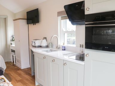 A kitchen area with white cabinets a sink toaster kettle and microwave at The Folly in Linton near Thresfield