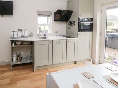 A kitchen with gray cabinets a sink a toaster kettle knives mounted on a wall and a dining table with glassware at The Folly in Linton near Thresfield