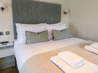 A bedroom with a bed with white pillows and beige blanket and folded white towels at The Folly in Linton near Thresfield