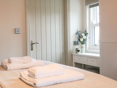 A bedroom with folded towels on the bed a door and a table with flowers by the window at The Folly in Linton near Thresfield