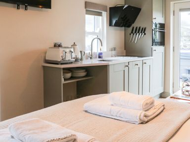 A kitchen area with a countertop toaster kettle sink and knives above the stove with folded towels on a bed at The Folly in Linton near Thresfield