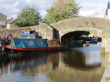 A canal boat moored next to a stone bridge over a canal with trees and buildings in the background at The Folly in Linton near Thresfield