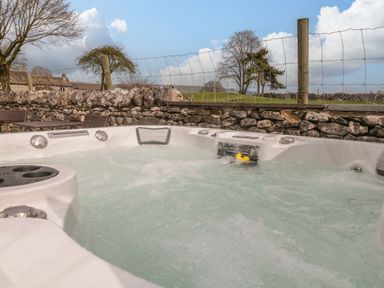 An outdoor hot tub with water bubbling near a stone wall and wire fence with trees beyond at The Folly in Linton near Thresfield