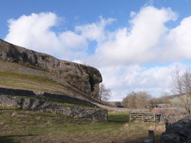 A rural landscape with stone walls trees and a rocky hill under a cloudy sky at The Folly in Linton near Thresfield