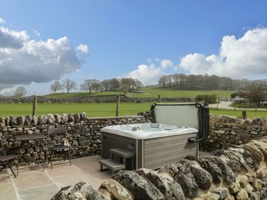 An outdoor patio area with a hot tub surrounded by stone walls and a view of green fields and trees at The Folly in Linton near Thresfield