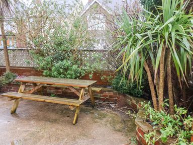 A wooden picnic table in a garden area with brick walls and various green plants at South Bay Beach House in Bridlington