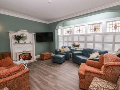 A living room with armchairs sofas a fireplace a television and stained glass windows at South Bay Beach House Bridlington