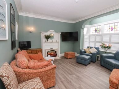 A sitting room with patterned sofas a white electric fireplace a wall mounted TV and windows with stained glass at South Bay Beach House in Bridlington