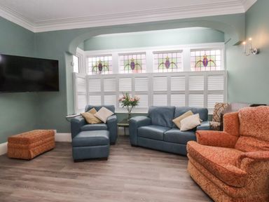 A living room with blue leather sofas orange patterned armchair and shuttered windows at South Bay Beach House in Bridlington