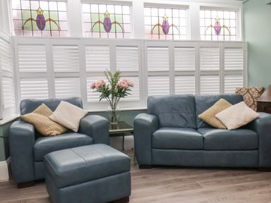 A living room with a blue armchair and sofa with cushions and a glass vase with flowers on a side table at South Bay Beach House in Bridlington