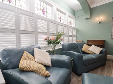 A sitting area with blue armchairs and cushions near white window shutters and a vase of flowers at South Bay Beach House in Bridlington