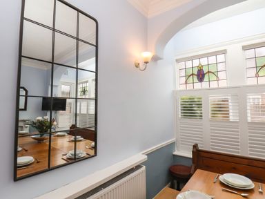 A dining area with a wooden table set with plates and cutlery a large grid mirror on the wall stained glass windows and a wall light at South Bay Beach House in Bridlington