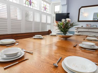 A dining room with a wooden table set with white plates bowls cutlery and a flower arrangement at South Bay Beach House Bridlington
