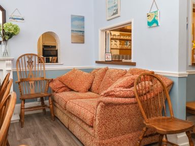 A seating area with an orange patterned sofa and wooden chairs in a room with light blue walls at South Bay Beach House in Bridlington