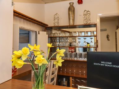 A bar area with glasses on shelves a vase of yellow flowers and a welcome sign at South Bay Beach House Bridlington