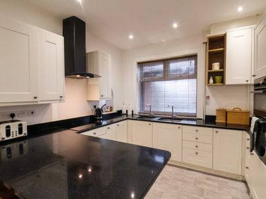 A kitchen with black countertops white cabinets a toaster kettle sink and window blinds at South Bay Beach House in Bridlington