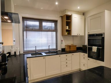 A kitchen with black countertops white cabinets a double sink a window with blinds a built in oven and shelves at South Bay Beach House in Bridlington
