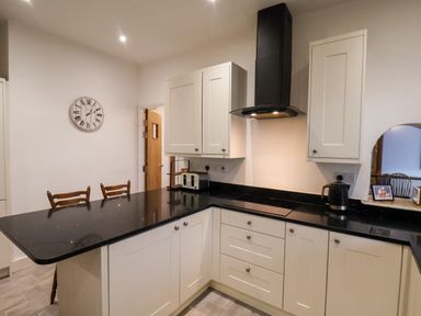 A kitchen with white cabinets black countertops a black range hood a toaster and a kettle at South Bay Beach House in Bridlington